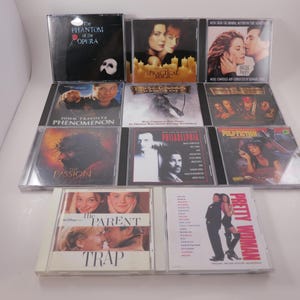 May include: A collection of compact discs featuring movie soundtracks and musical albums. Titles include "The Phantom of the Opera," "Magical Music," "Phenomenon," "Passion," "Pulp Fiction," "The Parent Trap," and "Pretty Woman."
