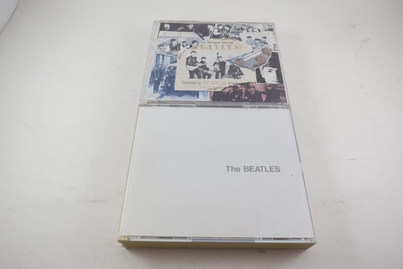 May include: Two CD cases. The top case features a collage of black and white images of The Beatles and the text "The Beatles 1962-1966". The bottom case is white with the band's name in gray text.