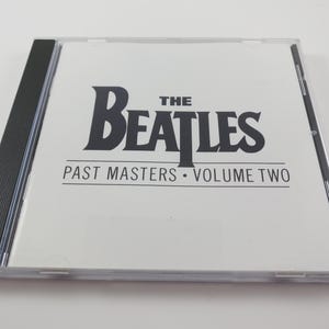 May include: A compact disc case featuring "The Beatles: Past Masters Volume Two" in black text on a white background. The CD case is clear with a black spine.