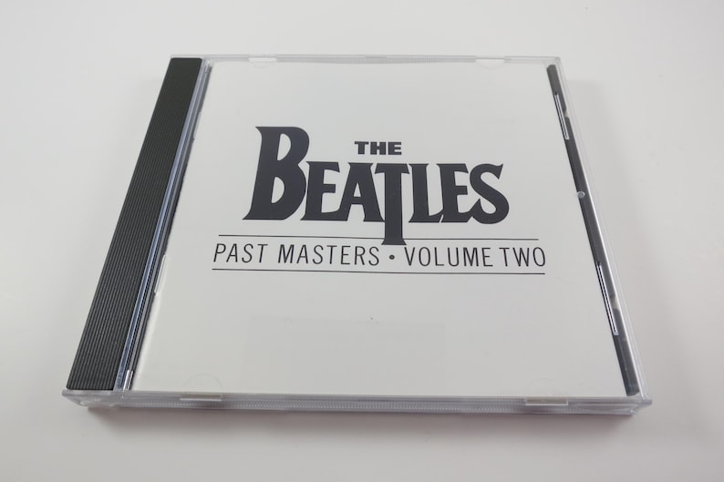 May include: A compact disc case featuring "The Beatles: Past Masters Volume Two" in black text on a white background. The CD case is clear with a black spine.