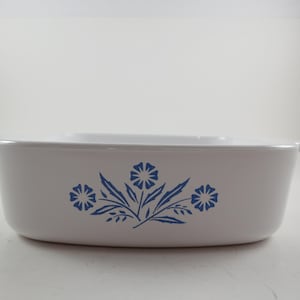 May include: White rectangular casserole dish with a blue floral design. The dish has two small handles and a lid. The floral design features three stylized flowers and leaves. A classic piece for baking and serving.