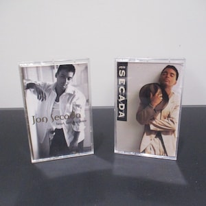 May include: Two cassette tapes in clear plastic cases featuring Jon Secada. The left case has a black and white photo of Jon Secada with the text "Jon Secada Heart, Soul & Voice". The right case has a color photo of Jon Secada with the text "Jon Secada".