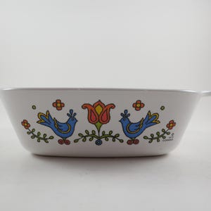 May include: White rectangular casserole dish with handles, decorated with blue birds, orange and yellow flowers, and a central red and orange tulip. The dish has a vintage, retro design.