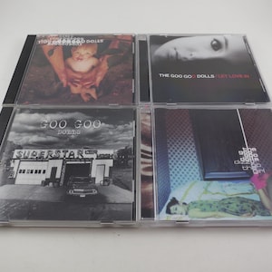 May include: Four CD cases featuring album art. The top left case shows a baby held in hands. The top right case has a woman's face. The bottom left case shows a black and white photo of a building. The bottom right case shows a person lying down.