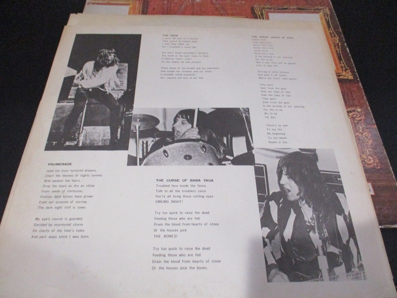 Op de afbeelding: Zwart-witfoto van een band die muziek maakt. De songteksten van de nummers "Promenade" en "The Curse of Baba Yaga" staan op de pagina afgedrukt. De songteksten bevatten de regels "Lead me from tortured dreams" en "Try too quick to raise the dead".