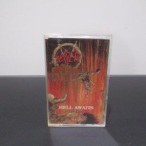 May include: A cassette tape featuring the Slayer band logo in red and the album title "Hell Awaits." The artwork depicts a fiery scene with figures and the band's name. The cassette is in a clear plastic case.