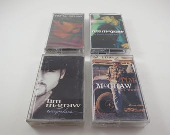 May include: Four cassette tapes featuring country music artist Tim McGraw. The tapes are in clear plastic cases with black and white photos of Tim McGraw on the front. The titles of the tapes are "Tim McGraw", "Everywhere", "A Place in the Sun", and "Everywhere I Want To Go".