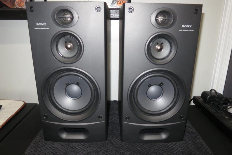 May include: Two black Sony 3-way speaker systems. Each speaker has a large central woofer, a mid-range speaker, and a tweeter. The speakers are rectangular with rounded edges and a small rectangular port at the bottom.