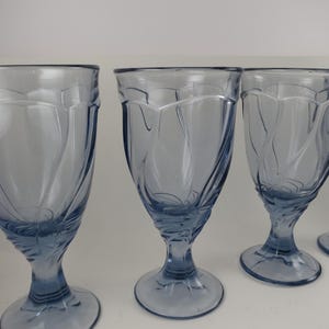 Pu&ograve; includere: Un set di calici in vetro azzurrato. Ogni calice presenta una coppa svasata con un motivo a spirale decorativo e un gambo. I bicchieri sono disposti in fila, mostrando la loro forma e il loro colore eleganti.