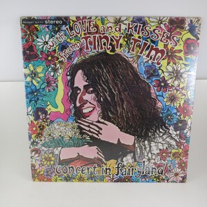 May include: A vintage vinyl record album cover featuring a portrait of Tiny Tim. The cover is decorated with colorful flowers and the text "With Love and Kisses From Tiny Tim" and "Concert in Fairyland".