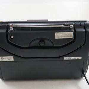 May include: A black portable radio with a silver antenna extended. The back of the radio features a control knob, a small information label, and a power cord. The radio is set against a white background.