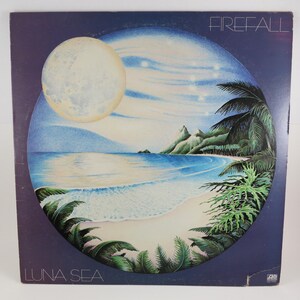 May include: Vintage vinyl record album cover for Firefall's "Luna Sea." The artwork features a full moon, a beach scene with palm trees, and the album title. The color palette includes blues, greens, and white.
