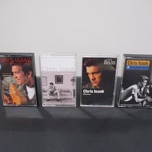 May include: Four cassette tapes by Chris Isaak. The tapes are in clear plastic cases with black trim. The titles are "Chris Isaak - San Francisco Days", "Chris Isaak -  His Greatest Hits", "Chris Isaak -  Silvertone", and "Chris Isaak -  Forever Yours (Best Of)".