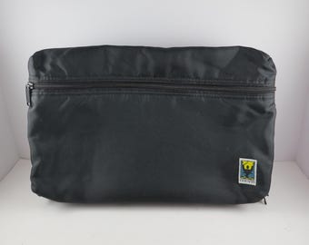 Può includere: Borsa da viaggio rettangolare nera con chiusura a cerniera. La borsa presenta una piccola toppa rettangolare con un design colorato nell'angolo in basso a destra. La borsa è realizzata in un materiale liscio, forse nylon.