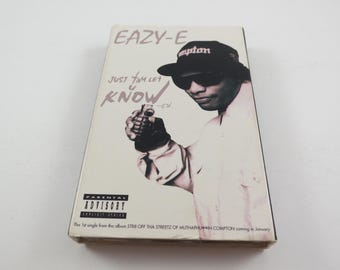 May include: A vintage Eazy-E cassette tape. The cover shows Eazy-E in a Compton hat and sunglasses, holding a grenade. Text includes "EAZY-E", "JUST TAM LET KNOW", and "PARENTAL ADVISORY EXPLICIT LYRICS".