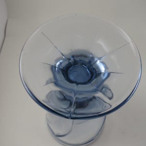 Pu&ograve; includere: Un calice di vetro trasparente con una coppa e uno stelo colorati di blu. La coppa ha una forma circolare con linee che si irradiano dal centro. Il calice &egrave; su una superficie bianca.