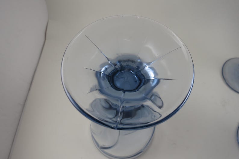 Pu&ograve; includere: Un calice di vetro trasparente con una coppa e uno stelo colorati di blu. La coppa ha una forma circolare con linee che si irradiano dal centro. Il calice &egrave; su una superficie bianca.