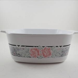 May include: White rectangular baking dish with a floral design. The dish features a band of gray and black with pink roses and green leaves. It has two handles on either side.