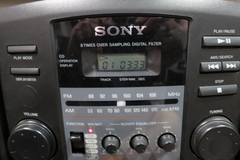 May include: Black Sony stereo system with a digital display showing the time. Features include FM/AM radio, CD player, and rotary equalizer. Buttons for play, pause, and tuning are visible.