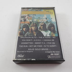 May include: A vintage cassette tape featuring the band Sweet. The album cover shows the band members with a cityscape background. The tracklist includes "Ballroom Blitz" and "The 6-Teens." The cassette is a Capitol Re-Issue.