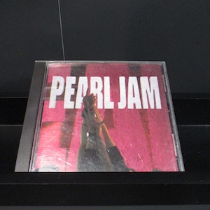 May include: A CD case with a pink background and the text "PEARL JAM" in white. The image shows a person's hands reaching up.