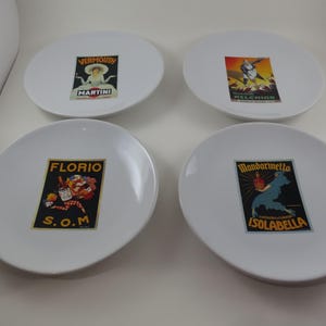 May include: Four white ceramic plates with vintage-style liquor advertisements. Each plate features a different design: "Vermouth Martini", "Relchior", "Florio S.O.M.", and "Mandarinetta Isolabella". The plates are round and have a simple, clean design.