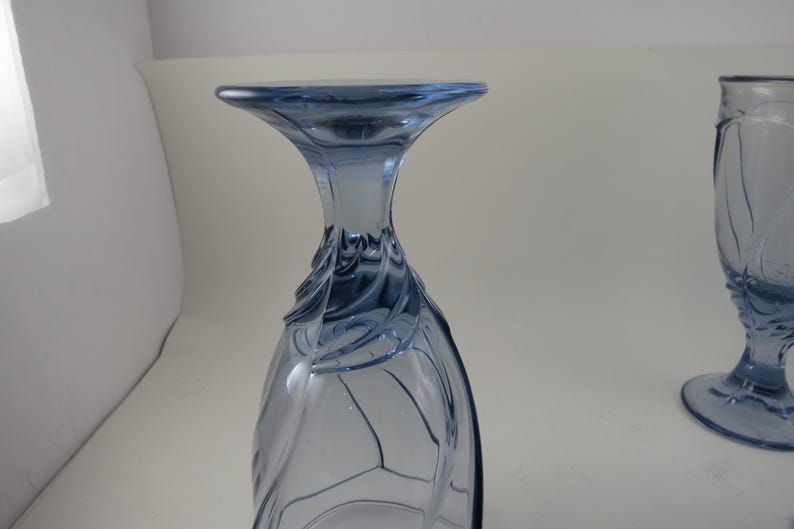 Pu&ograve; includere: Due calici di vetro blu. Il calice a sinistra &egrave; capovolto, mostrando il bordo svasato e il design decorativo a spirale. L'altro calice &egrave; in posizione verticale, con un design simile. Entrambi sono su sfondo bianco.