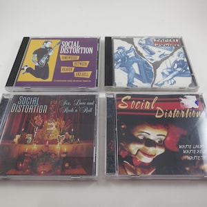 May include: Four Social Distortion CD albums. The album covers feature various designs, including a figure playing guitar, illustrations, and a doll-like face. The text on the covers includes album titles and band names.