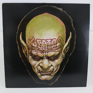 May include: Album cover featuring a grotesque, green-skinned creature with large ears and the word "KREATOR" in red lettering across its forehead. The artwork is set against a black background, creating a striking contrast.