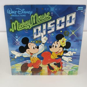 May include: A vintage Walt Disney Productions record album cover featuring Mickey Mouse and Minnie Mouse dancing. The album title is "Mickey Mouse Disco" in a neon green and white font against a blue background with stars and disco lights.