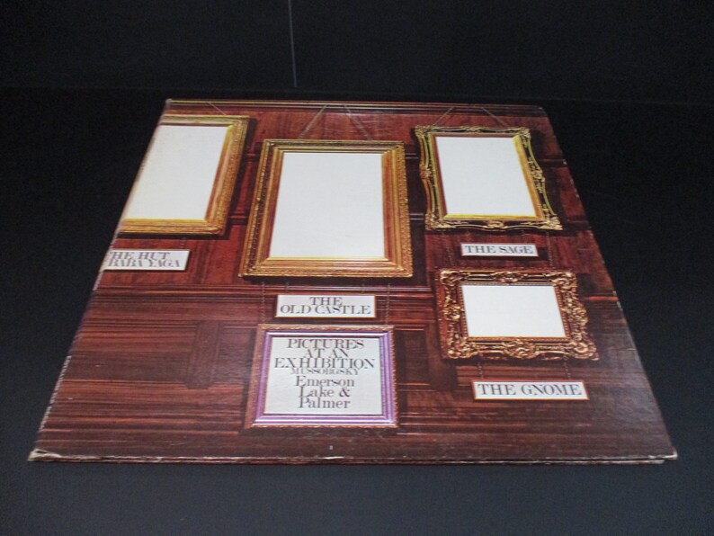 May include: A vintage vinyl record album cover featuring a wood-paneled wall with five ornate gold picture frames. The album title is "Pictures at an Exhibition" by Modest Mussorgsky, Emerson, Lake & Palmer.