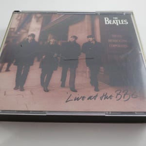 May include: A CD case featuring The Beatles' album "Live at the BBC." The cover art shows the band members walking on a street. The album title and band name are visible on the cover.