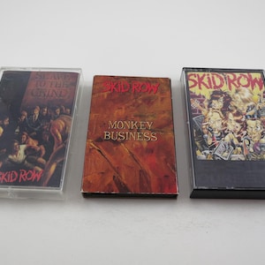 May include: Three cassette tapes with black cases and colourful artwork. The tapes are labelled "Skid Row" and feature the titles "Slave to the Grind", "Monkey Business", and "Skid Row".