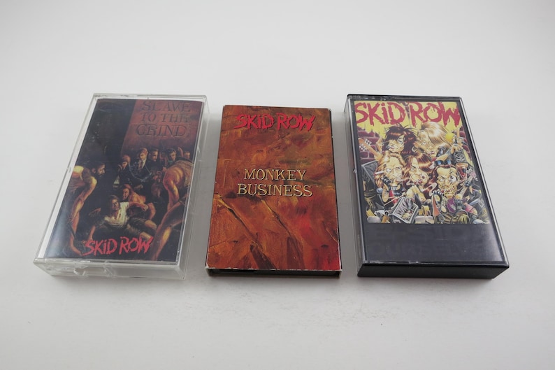 May include: Three cassette tapes with black cases and colourful artwork. The tapes are labelled "Skid Row" and feature the titles "Slave to the Grind", "Monkey Business", and "Skid Row".