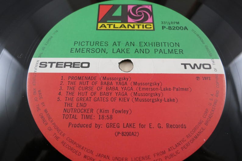 Puede incluir: Un disco de vinilo vintage con una etiqueta verde y roja que presenta el &aacute;lbum "Pictures at an Exhibition" de Emerson, Lake and Palmer. La etiqueta incluye los t&iacute;tulos de las pistas y el logotipo de Atlantic Records.