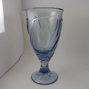 Pu&ograve; includere: Un bicchiere alto, azzurro chiaro, con un design decorativo a spirale. Il bicchiere ha una parte superiore ampia e svasata e una base a stelo. Il design presenta linee curve e motivi floreali. Il bicchiere &egrave; in vetro trasparente.