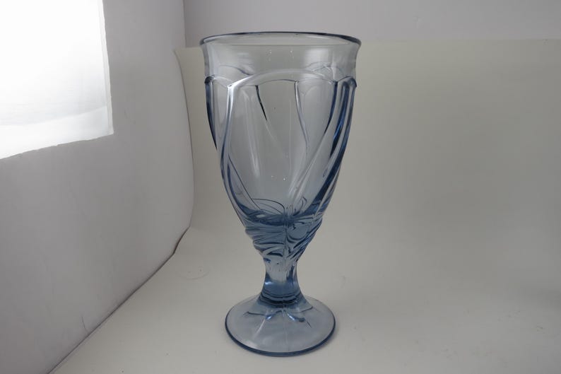 Pu&ograve; includere: Un bicchiere alto, azzurro chiaro, con un design decorativo a spirale. Il bicchiere ha una parte superiore ampia e svasata e una base a stelo. Il design presenta linee curve e motivi floreali. Il bicchiere &egrave; in vetro trasparente.