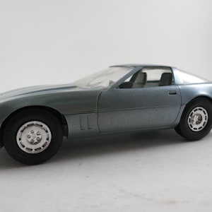 May include: A metallic blue toy car with black tires and silver rims. The car has a sleek, aerodynamic design with a transparent windshield and a two-seat interior. The car is a model of a sports car.