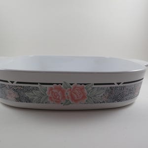 May include: White rectangular baking dish with handles. The dish features a decorative band with a floral pattern of pink roses and green leaves. The band is bordered by black lines.