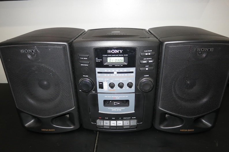 May include: Black Sony stereo boombox with two speakers and a central unit. The unit has a CD player, cassette player, and radio. The speakers are labeled "Mega Bass". The display shows "01:03:06".