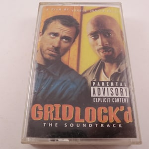 May include: A vintage cassette tape for the soundtrack of the film "Gridlock'd." The cover features images of two men, with the title in orange and the parental advisory warning. The cassette is in a clear plastic case.