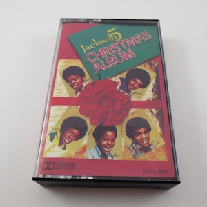 May include: A cassette tape with a red, green, and white design. The front of the tape features a picture of the Jackson 5 with the text "Jackson 5 Christmas Album".
