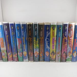 May include: A collection of seventeen Walt Disney VHS tapes arranged in a row, featuring titles such as Peter Pan, Beauty and the Beast, The Rescuers, Lady and the Tramp, The Fox and the Hound, Sleeping Beauty, Cinderella, The Jungle Book, and Aladdin.