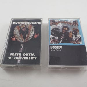 May include: Two vintage cassette tapes. One features Bootsy Collins' album "Fresh Outta 'P' University" with a black background and a colorful image. The other is Bootsy's "Ultra Wave" album with a black background and a collage of images.