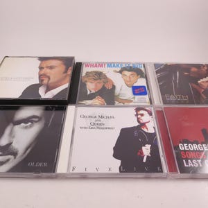 May include: A collection of music CDs featuring George Michael and Wham! album covers. The album covers are in clear plastic cases and feature images of the artists. Titles include "Faith", "Older", and "Five Live".