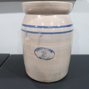 May include: A vintage stoneware crock with a beige glaze and two blue stripes. The crock features an oval label with the text "Marshall Pottery, Inc. 2 Marshall, Texas."