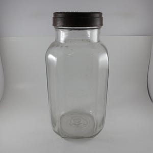 May include: A clear glass jar with a rectangular body and rounded corners, featuring a dark brown screw-top lid. The container has a wide mouth and a smooth, transparent surface, showcasing a simple and functional design for storage purposes.