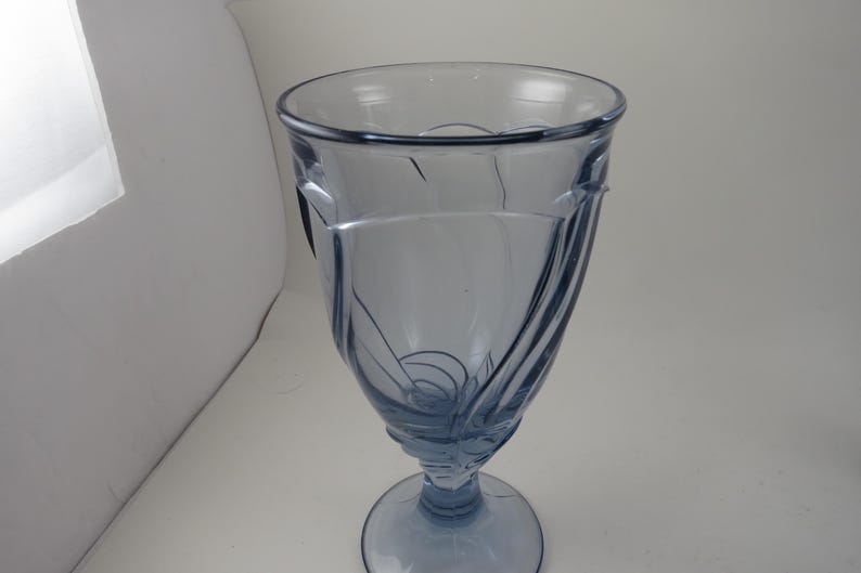 Pu&ograve; includere: Un calice di vetro colorato di blu, di forma alta, con un design decorativo. Il vetro presenta una coppa svasata, uno stelo e una base circolare. Il design comprende linee curve e spirali.