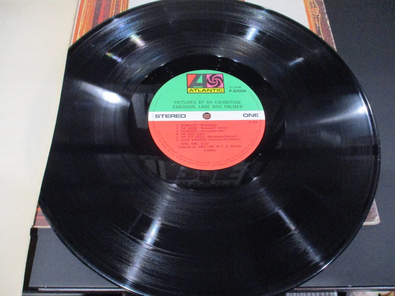 Op de afbeelding: Zwarte vinylplaat met een groen en rood label. Het label zegt "Pictures at an Exhibition, Emerson, Lake and Palmer" en "Stereo, E&eacute;n".