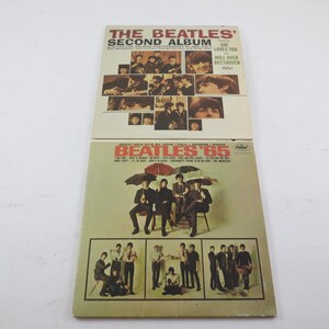 May include: Two vintage vinyl record albums. The top album is "The Beatles' Second Album" with images of the band. The bottom album is "Beatles '65" with the band under umbrellas and other images.